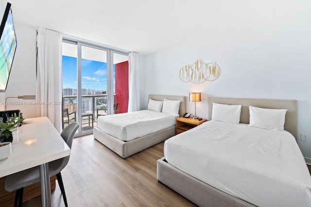 bedroom with a view of city, wood finished floors, floor to ceiling windows, and access to outside