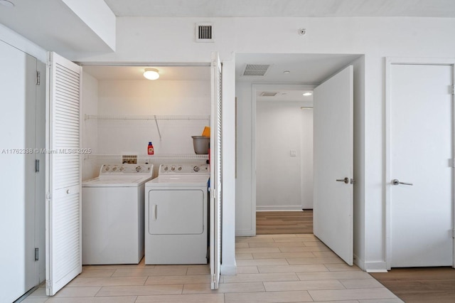 clothes washing area featuring laundry area, light wood-type flooring, visible vents, and separate washer and dryer