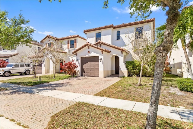 mediterranean / spanish-style home featuring stucco siding, a tiled roof, decorative driveway, and a garage