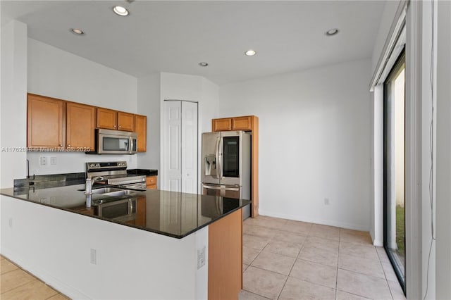 kitchen featuring light tile patterned floors, brown cabinetry, a peninsula, a sink, and appliances with stainless steel finishes