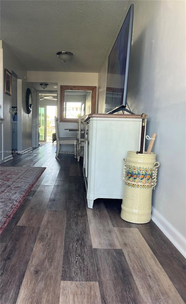 hall featuring a textured ceiling, baseboards, and wood finished floors