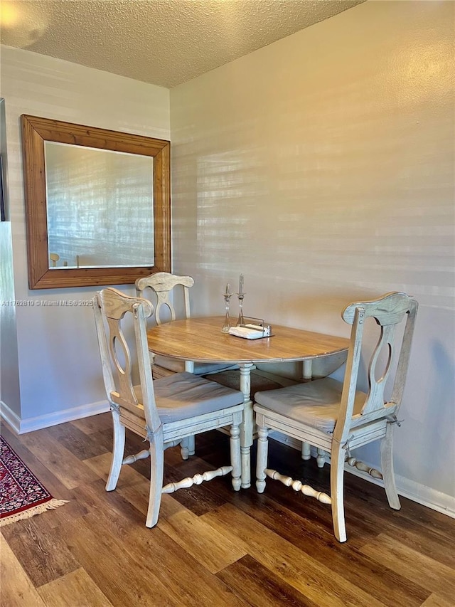 dining space featuring a textured ceiling, baseboards, and wood finished floors