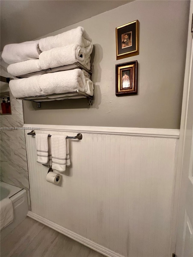 bathroom with a washtub, wood finished floors, and wainscoting