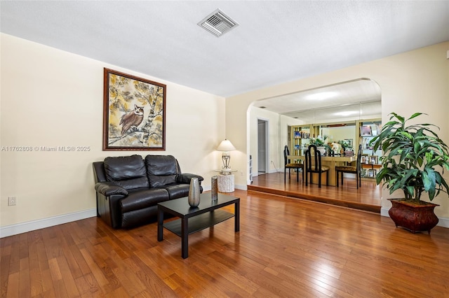 living area featuring hardwood / wood-style flooring, arched walkways, visible vents, and baseboards