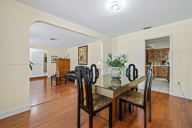 dining room featuring arched walkways, visible vents, and light wood finished floors