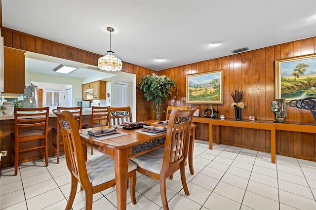 dining space with light tile patterned floors, visible vents, and wood walls