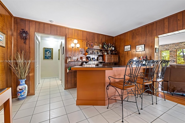 bar featuring light tile patterned floors, wooden walls, and a dry bar