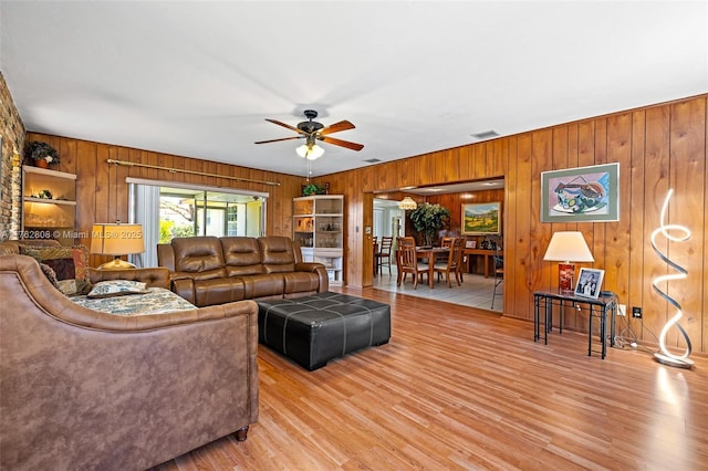 living area with wooden walls, visible vents, light wood-style flooring, and ceiling fan