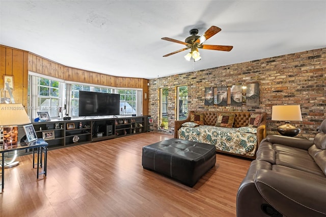 living room with wood finished floors, brick wall, and ceiling fan