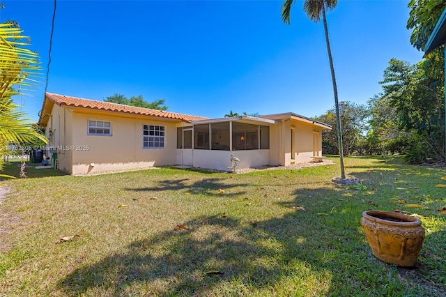 back of property with a tiled roof, stucco siding, a lawn, and a sunroom