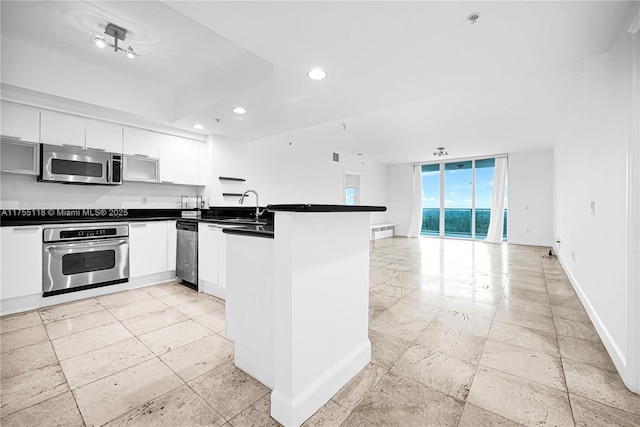 kitchen with dark countertops, baseboards, appliances with stainless steel finishes, a peninsula, and a sink