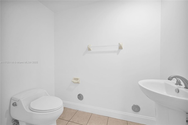 half bathroom featuring tile patterned floors, toilet, baseboards, and a sink