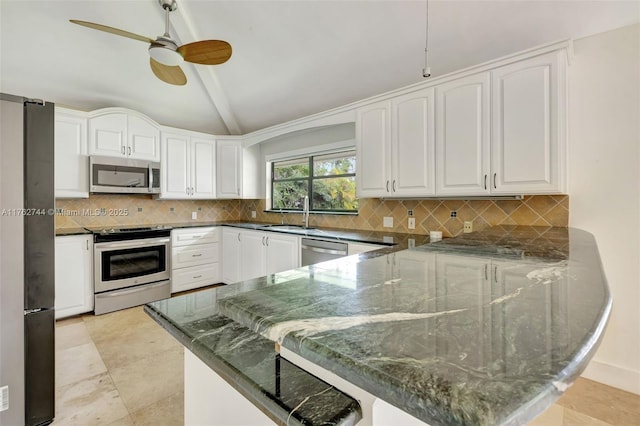 kitchen featuring vaulted ceiling, appliances with stainless steel finishes, a peninsula, white cabinets, and a sink