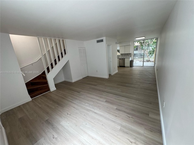 unfurnished living room with stairs, baseboards, visible vents, and light wood finished floors