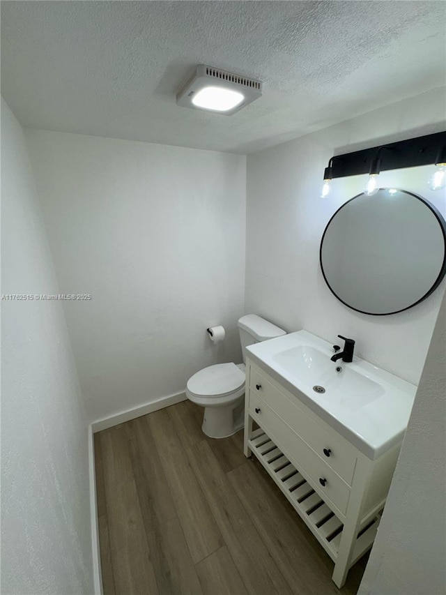 half bathroom with vanity, toilet, wood finished floors, and a textured ceiling