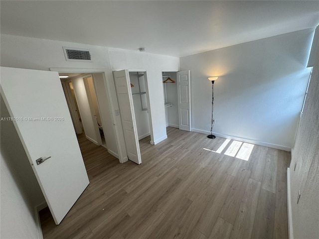 unfurnished bedroom with wood finished floors, visible vents, a closet, and baseboards