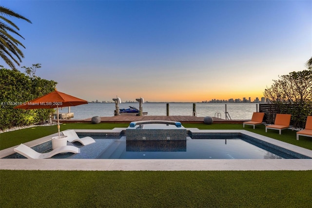 pool at dusk with a yard, a water view, an in ground hot tub, and a boat dock