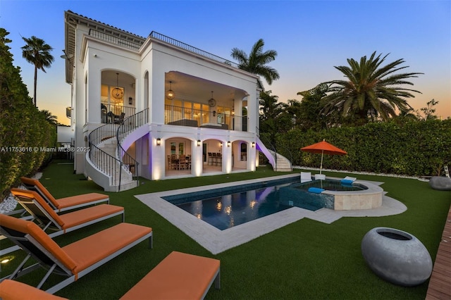 back of property at dusk featuring stairway, a patio, a lawn, and a balcony