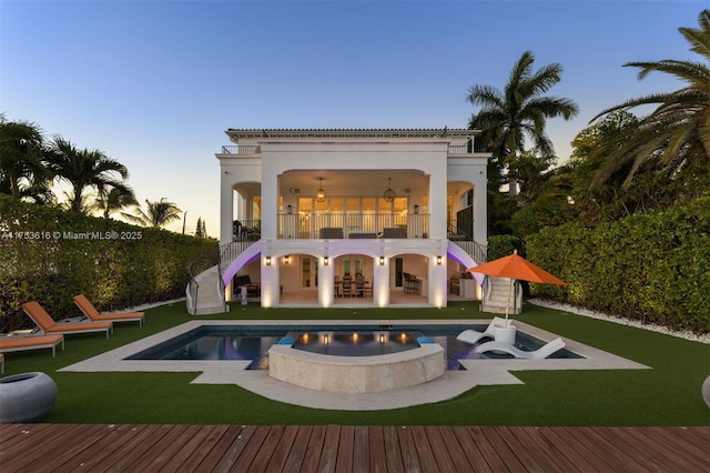 back of property at dusk featuring a yard, stairway, stucco siding, and a balcony