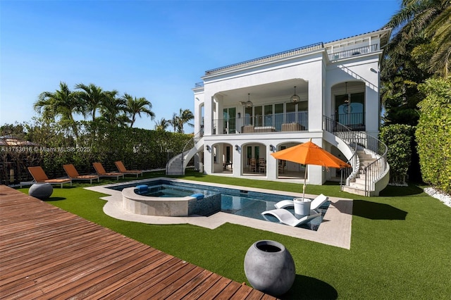 back of house with stairs, a balcony, a yard, an in ground hot tub, and a patio