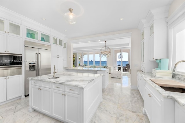 kitchen with light stone countertops, built in appliances, white cabinets, marble finish floor, and a sink