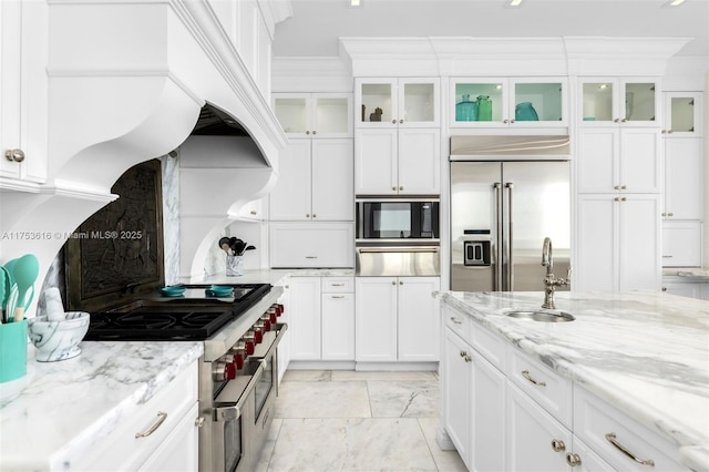 kitchen featuring built in appliances, custom range hood, ornamental molding, white cabinetry, and a sink