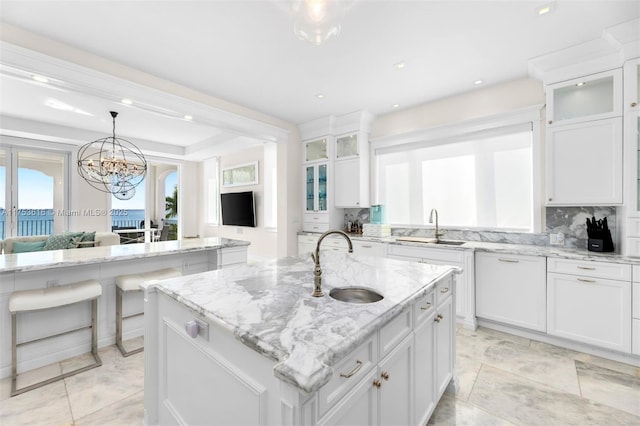 kitchen with a sink, glass insert cabinets, an island with sink, and white cabinets