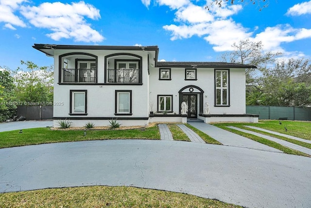 view of front of property with stucco siding, a front yard, a balcony, and fence