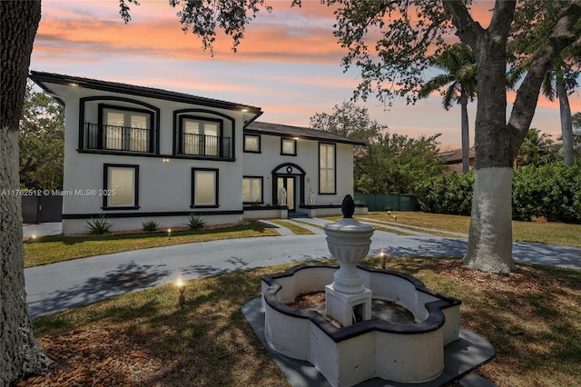 view of front facade with stucco siding, a balcony, and a lawn
