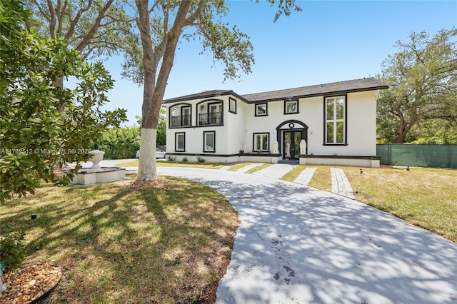 view of front of home with fence, a front lawn, stucco siding, and curved driveway