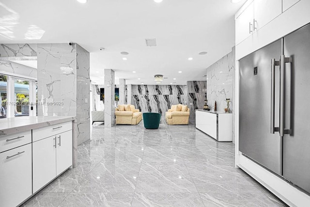 interior space featuring stone wall, visible vents, white cabinetry, high quality fridge, and marble finish floor