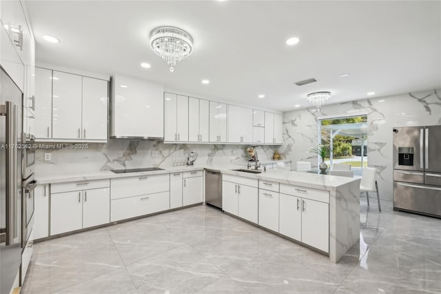 kitchen with an inviting chandelier, stainless steel appliances, marble finish floor, white cabinetry, and a peninsula