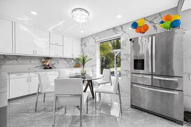 kitchen with stone wall, marble finish floor, stainless steel fridge with ice dispenser, and light countertops