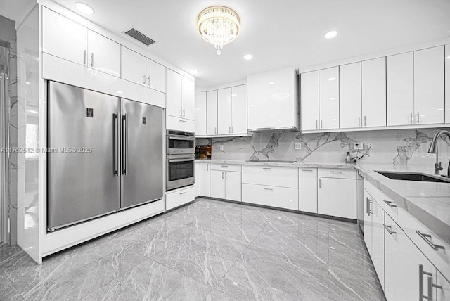 kitchen featuring light stone counters, visible vents, a sink, stainless steel appliances, and white cabinetry