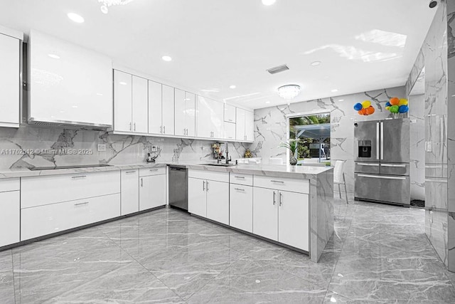 kitchen with visible vents, marble finish floor, stainless steel appliances, a peninsula, and stone wall