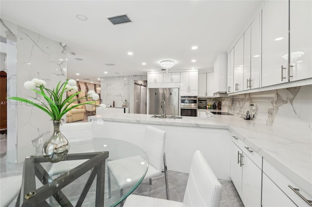 kitchen with light stone countertops, visible vents, white cabinets, and stainless steel appliances