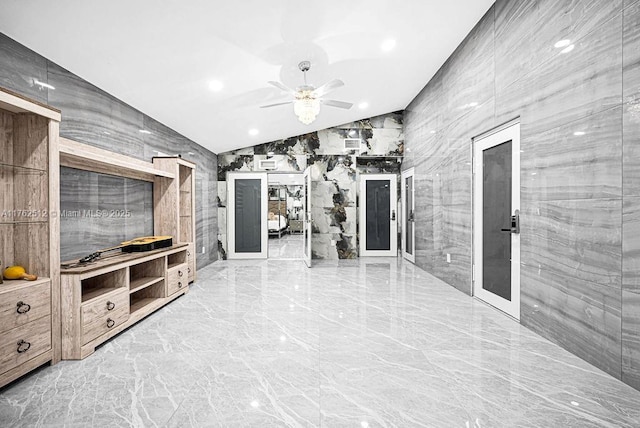 living room featuring marble finish floor, tile walls, a ceiling fan, and vaulted ceiling