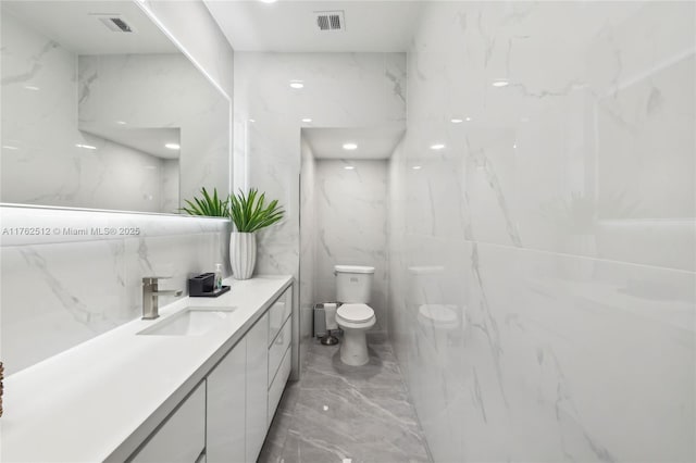 bathroom featuring marble finish floor, tile walls, toilet, vanity, and visible vents