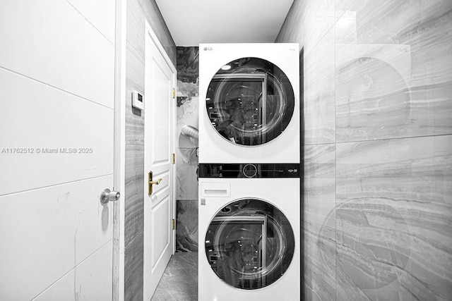 laundry room with laundry area, marble finish floor, stacked washing maching and dryer, and tile walls