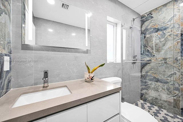 bathroom featuring visible vents, toilet, tile walls, a shower stall, and vanity