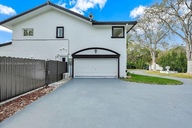 view of side of property featuring stucco siding, a garage, driveway, and fence