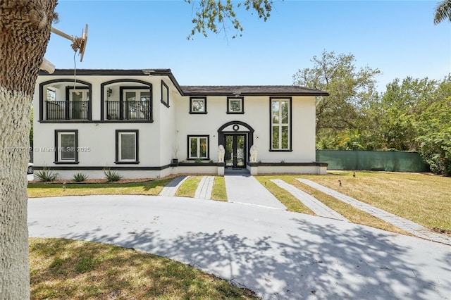 view of front of home with a front yard, stucco siding, french doors, and a balcony