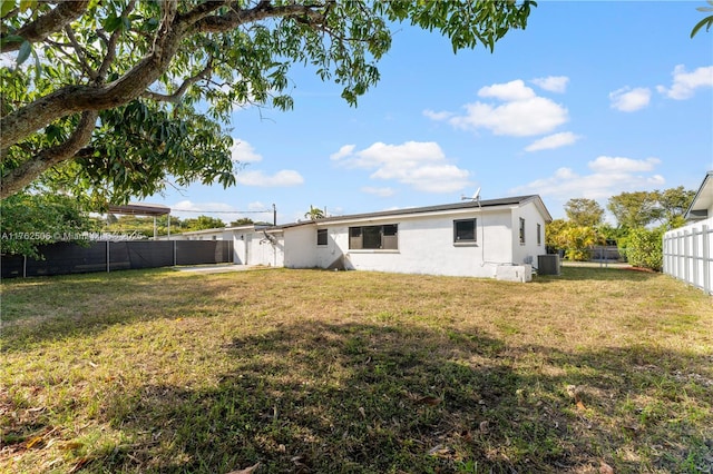 rear view of house featuring cooling unit, a fenced backyard, a lawn, and stucco siding