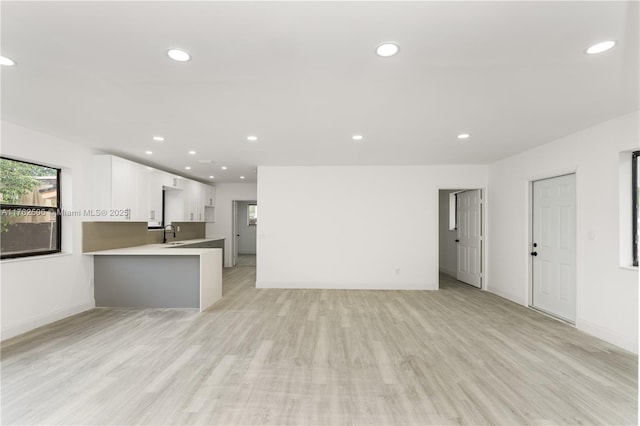 unfurnished living room featuring baseboards, recessed lighting, light wood-style floors, and a sink