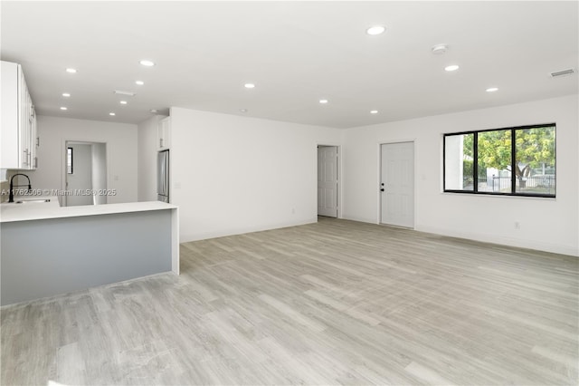 unfurnished living room featuring visible vents, baseboards, light wood-type flooring, recessed lighting, and a sink