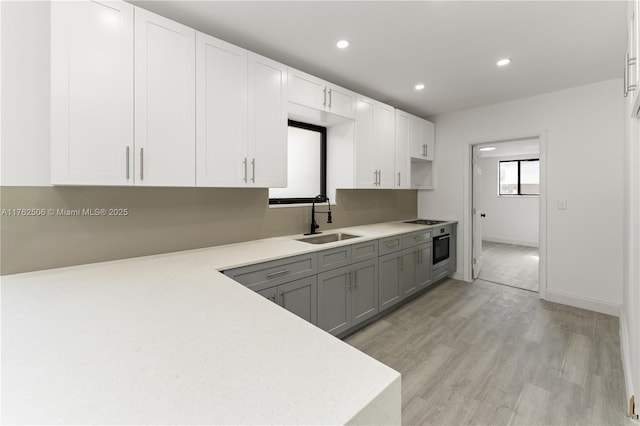 kitchen with light wood-type flooring, light countertops, stainless steel oven, gray cabinets, and a sink