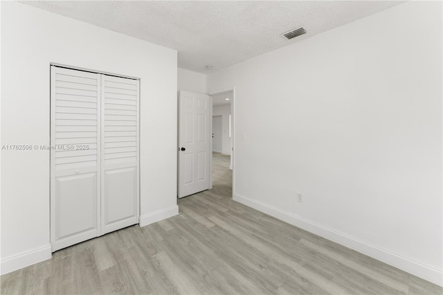 unfurnished bedroom with visible vents, baseboards, a textured ceiling, and light wood-style flooring