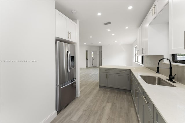 kitchen featuring a sink, light wood-style floors, stainless steel fridge with ice dispenser, and white cabinetry