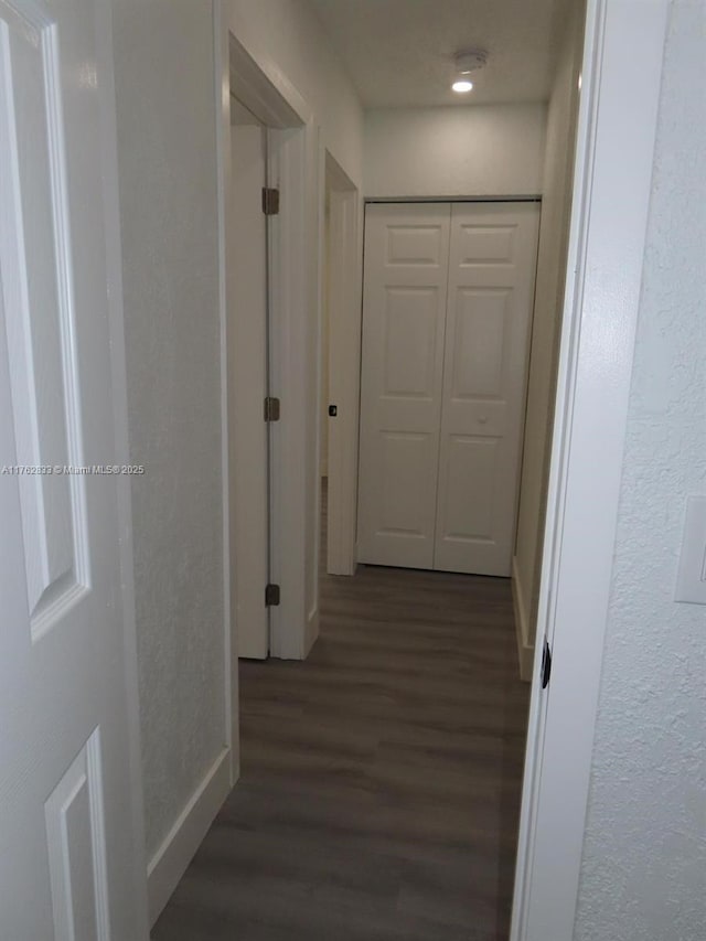 corridor featuring baseboards and dark wood-style floors