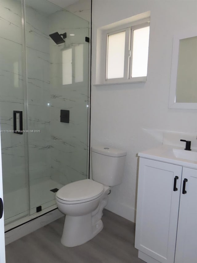 bathroom with vanity, toilet, wood finished floors, and a marble finish shower